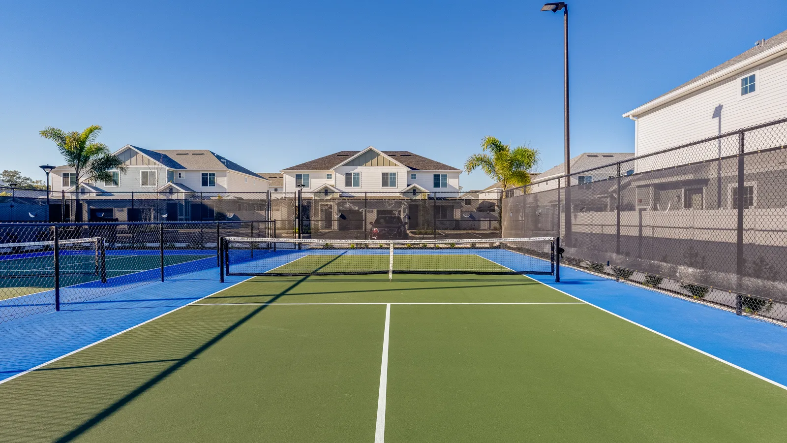 Pickleball courts with shaded black fencing and newly painted courts. Community sidewalk facing pond with green grass and trees. Apartments in Orlando with a view of beautiful landscape. New pet-friendly apartment homes for rent with private fenced backyards in Kissimmee, FL, near Orlando, FL with pickle ball, dog park, gym, and gated community. *No breed or weight restrictions. Yardly Bellalago