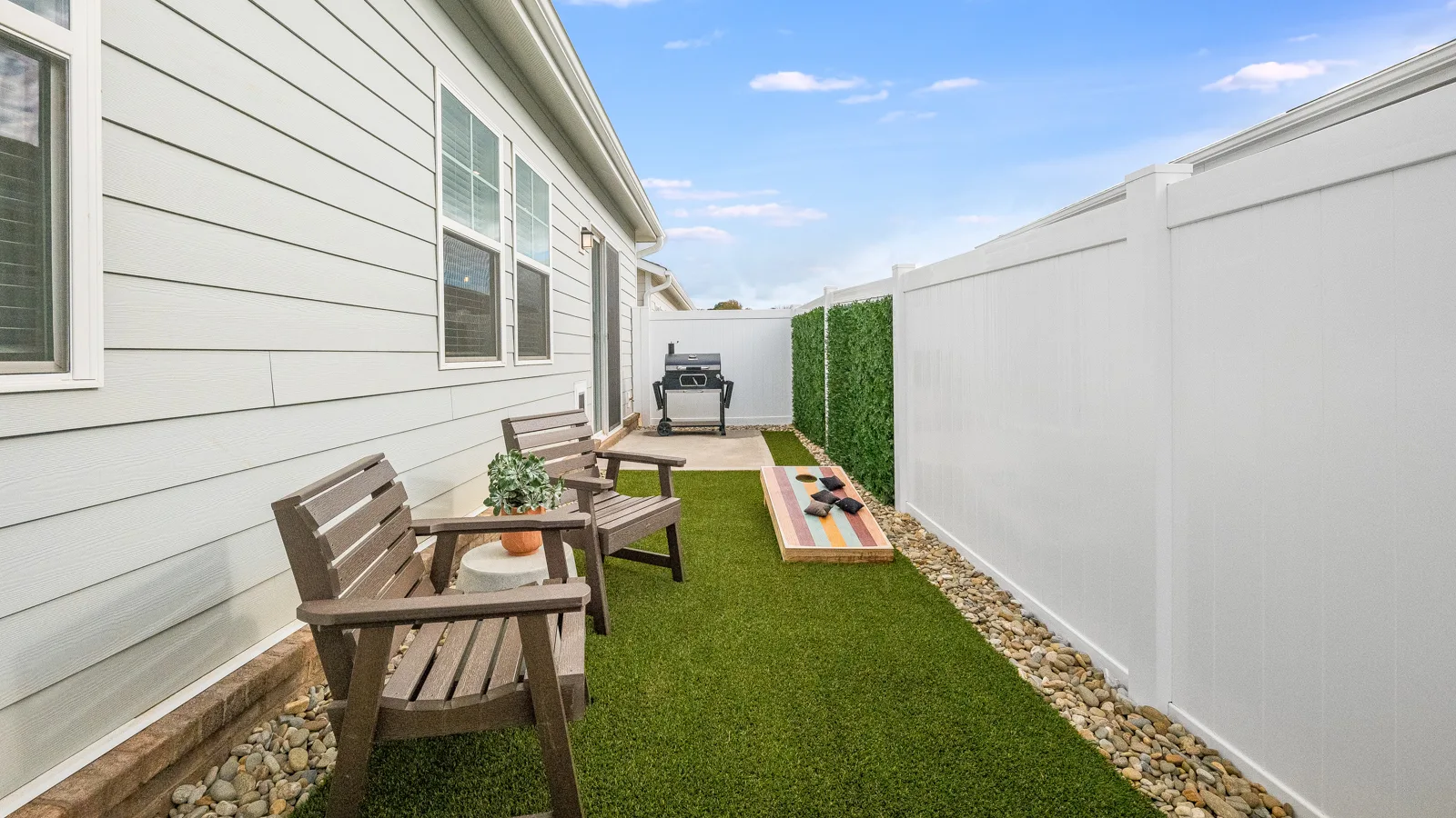 Photo of backyard with permanent landscaping featuring granite pebbles and astro turf with patio furniture. New pet-friendly apartment homes for rent with private fenced backyards in Monroe, NC, near Charlotte, NC with pool, dog park, gym, and gated community. *No breed or weight restrictions.