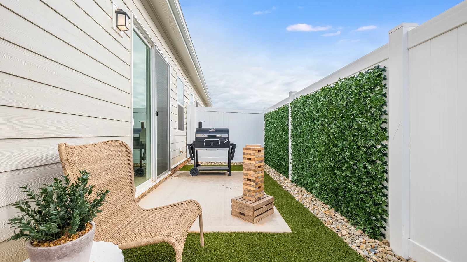 Photo of backyard with permanent landscaping featuring granite pebbles and astro turf with patio furniture. New pet-friendly apartment homes for rent with private fenced backyards in Monroe, NC, near Charlotte, NC with pool, dog park, gym, and gated community. *No breed or weight restrictions.