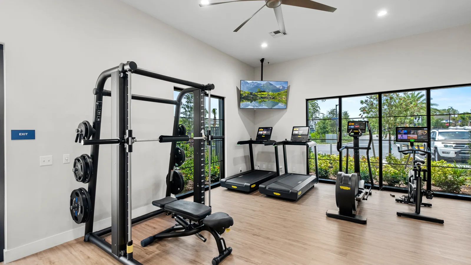 Artisan lakes shot of gym with large windows looking into all of the tropical foliage outside. New pet-friendly apartment homes for rent with private fenced backyards Arizona, Texas, Florida, and North Carolina with pool, pickleball, dog park, gym, clubhouse and gated community. *No breed or weight restrictions.