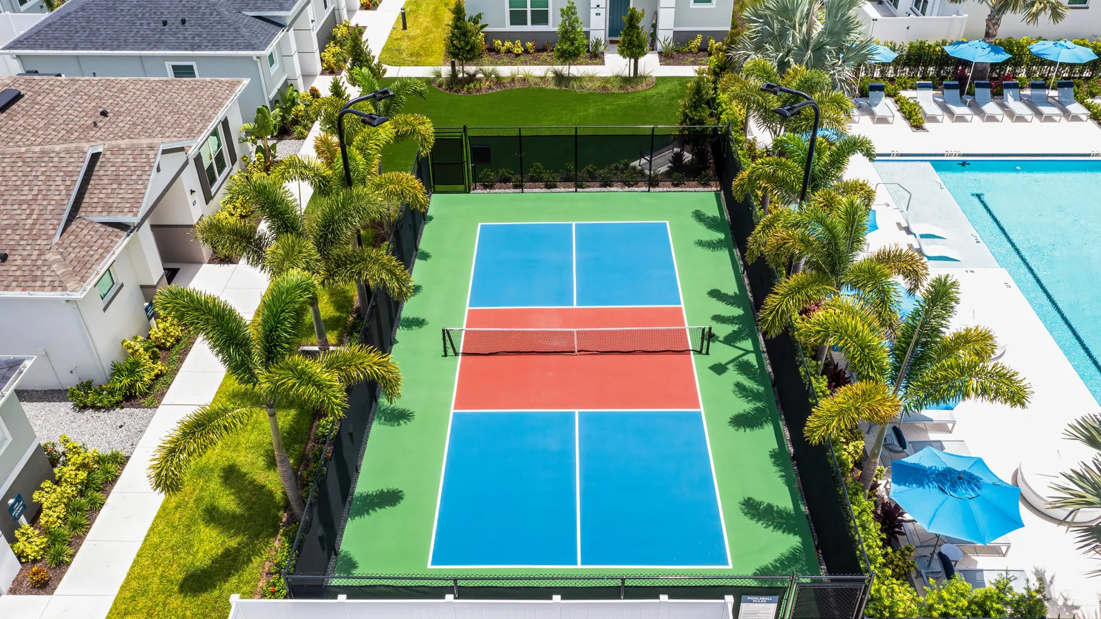 Artisan lakes arial shot of pickleball court surrounded by palm trees and privacy fencing. New pet-friendly apartment homes for rent with private fenced backyards Arizona, Texas, Florida, and North Carolina with pool, pickleball, dog park, gym, clubhouse and gated community. *No breed or weight restrictions.