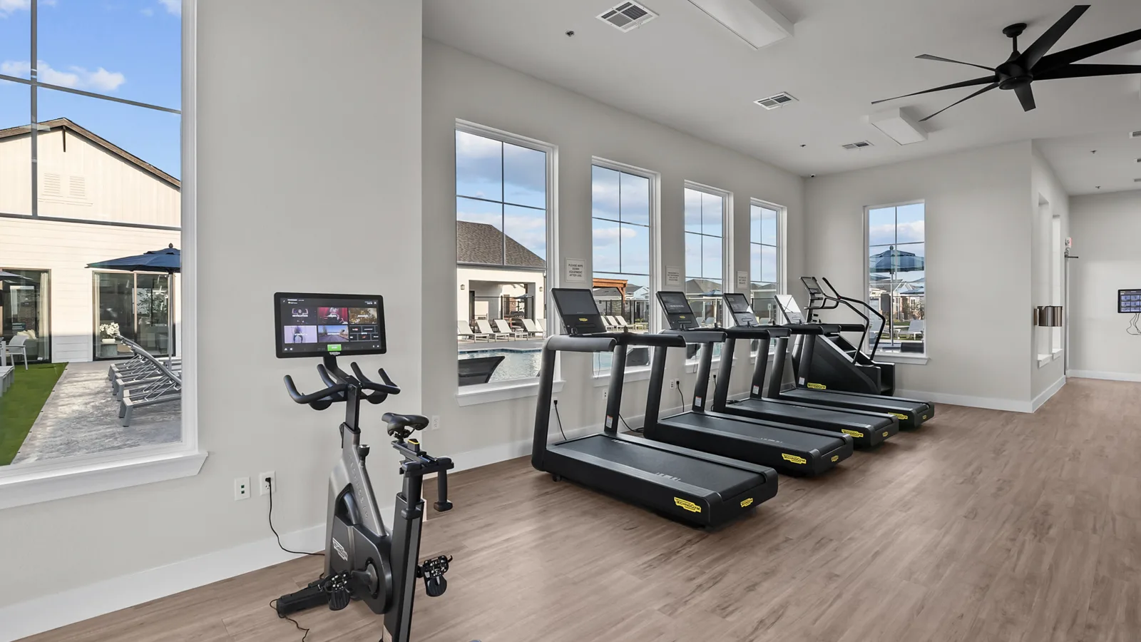 interior photo of Yardly cypress gym of treadmills and bikes. blue sunny sky outside by pool. New pet-friendly apartment homes for rent with private fenced backyards Arizona, Texas, Florida, and North Carolina with pool, pickleball, dog park, gym, clubhouse and gated community. *No breed or weight restrictions.